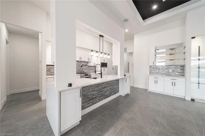 Kitchen with pendant lighting, white cabinetry, sink, and a towering ceiling