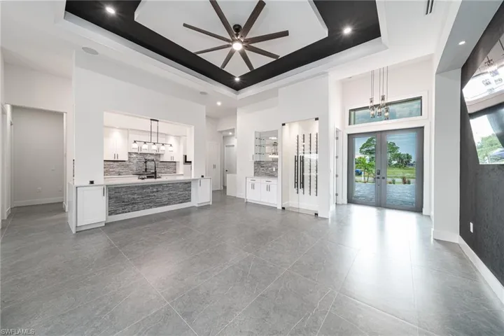 Unfurnished living room with ceiling fan with notable chandelier, french doors, sink, and a tray ceiling