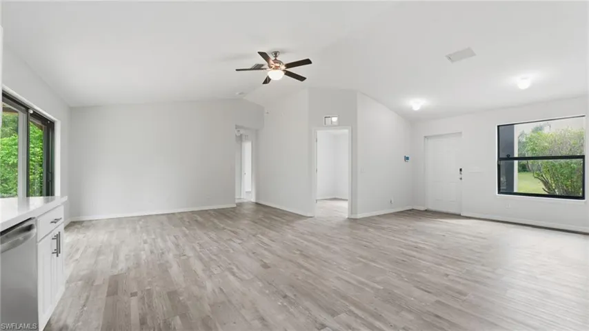 Unfurnished living room with plenty of natural light, light wood finished floors, ceiling fan, and vaulted ceiling