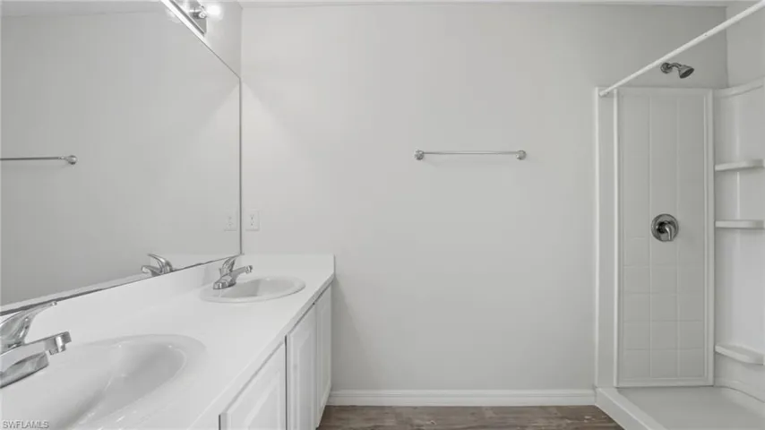 Full bath featuring a stall shower, double vanity, and dark wood-style flooring