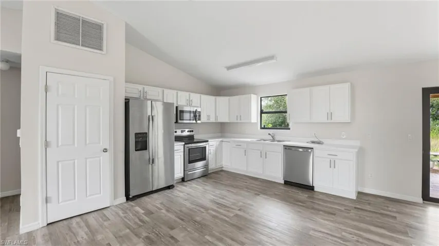 Kitchen with lofted ceiling, stainless steel appliances, white cabinets, light countertops, and light wood-style flooring