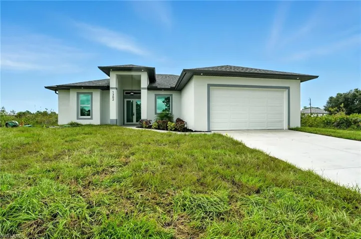 Prairie-style home featuring a garage, concrete driveway, stucco siding, and a front yard