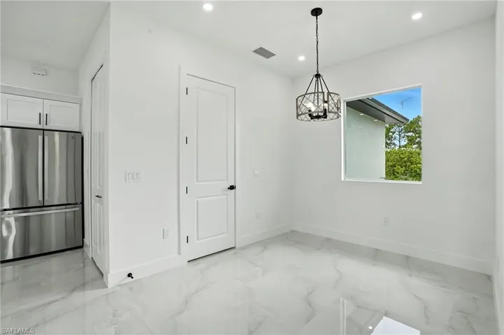 Kitchen featuring tasteful backsplash, white cabinetry, a kitchen island with sink, hanging light fixtures, and stainless steel appliances
