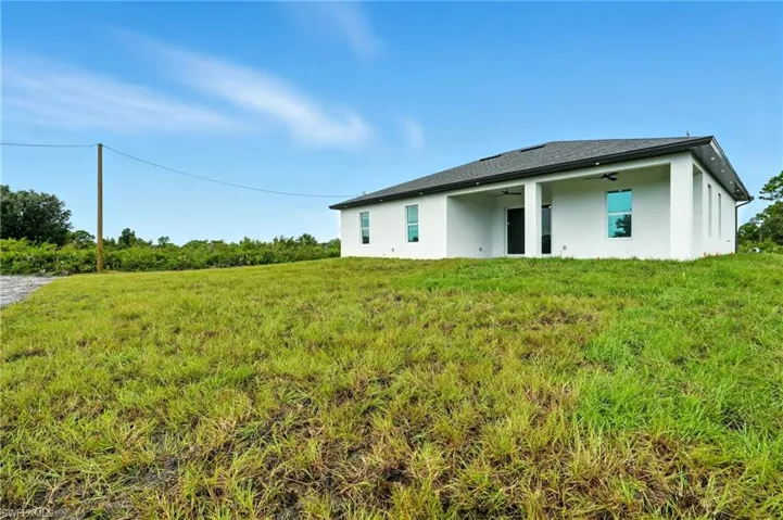 Rear view of house featuring stucco siding, a patio area, ceiling fan, and a lawn