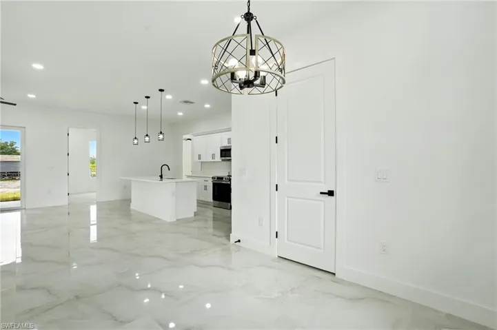 Kitchen featuring light marble finish floors, appliances with stainless steel finishes, hanging light fixtures, white cabinets, and light stone countertops
