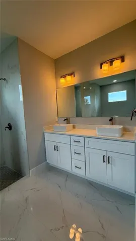 Bathroom featuring double vanity, a marble finish shower, and light marble finish flooring