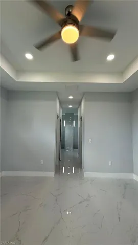 Unfurnished room with a tray ceiling, recessed lighting, light marble finish floors, and ceiling fan
