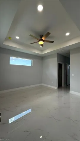 Empty room featuring a raised ceiling, recessed lighting, light marble finish floors, and a ceiling fan