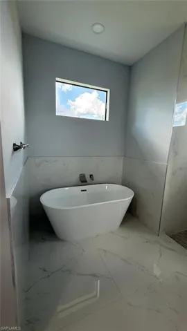 Full bath with a wainscoted wall, tile walls, a freestanding tub, and marble finish floors