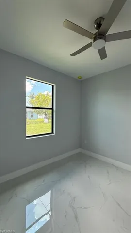 Spare room with marble finish floors and a ceiling fan