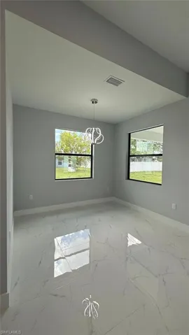 Empty room with light marble finish floors, healthy amount of natural light, and a chandelier