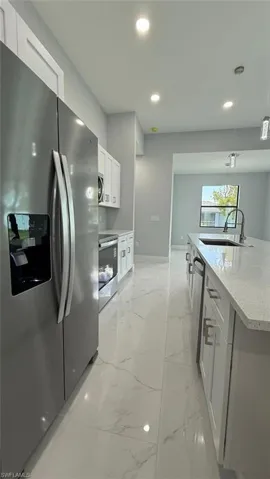 Kitchen with stainless steel appliances, decorative light fixtures, white cabinets, light stone counters, and light marble finish flooring