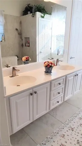 Bathroom with double vanity, light tile patterned floors, and a shower