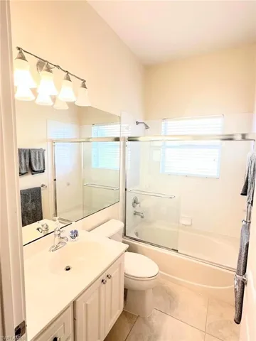 Full bath with vanity, shower / bath combination with glass door, and light tile patterned floors