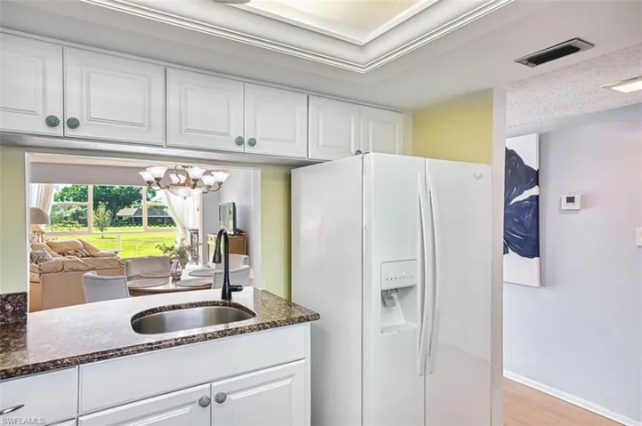 Kitchen featuring white refrigerator with ice dispenser, white cabinetry, dark stone countertops, and a chandelier