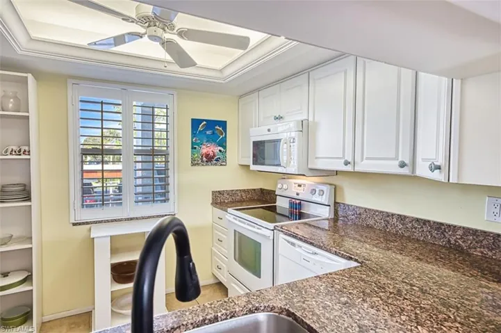 Kitchen with white cabinetry, white appliances, a ceiling fan, dark stone countertops, and crown molding