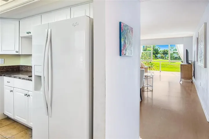 Kitchen with white fridge with ice dispenser, white cabinets, and dark stone countertops