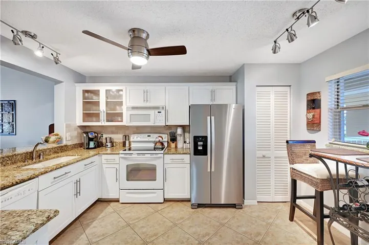 Kitchen featuring light tile patterned floors, glass insert cabinets, white cabinets, a sink, and white appliances