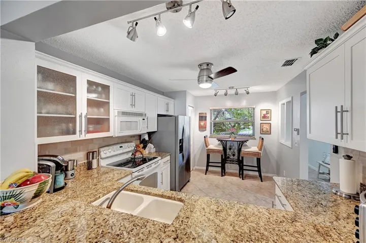 Kitchen with white appliances, a sink, visible vents, white cabinets, and glass insert cabinets