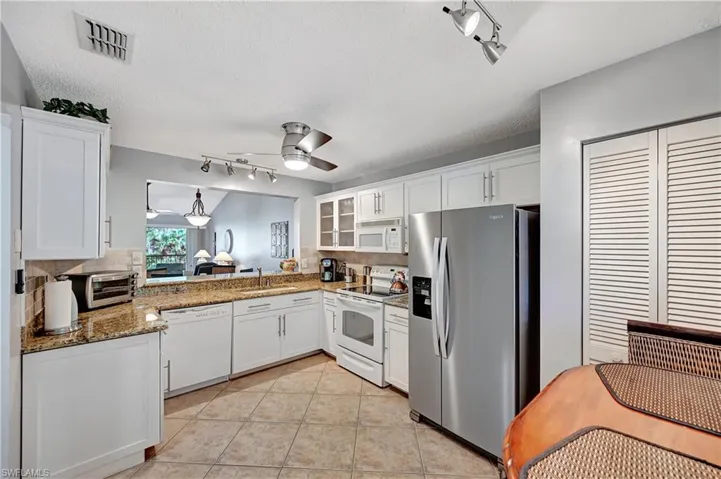 Kitchen featuring white appliances, tasteful backsplash, visible vents, ceiling fan, and white cabinetry
