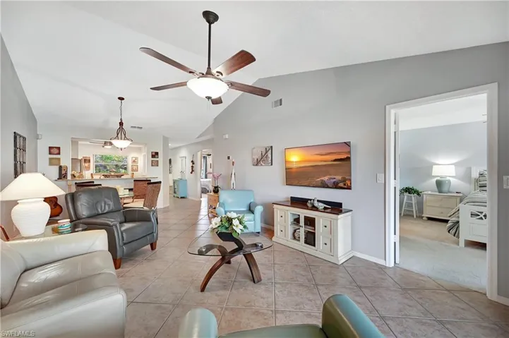 Living room with light tile patterned floors, ceiling fan, visible vents, baseboards, and vaulted ceiling