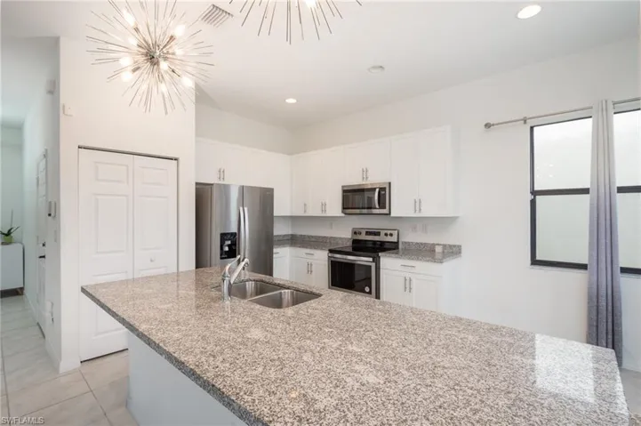 Kitchen with appliances with stainless steel finishes, white cabinets, decorative light fixtures, sink, and a chandelier
