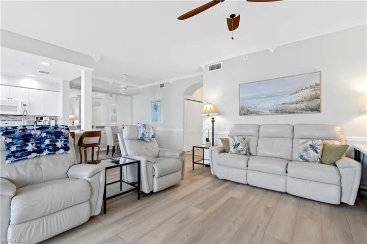 Living room with ceiling fan, light wood-type flooring, arched walkways, and ornamental molding