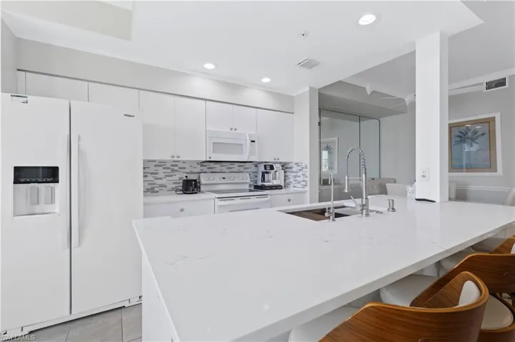 Kitchen with white appliances, white cabinets, a breakfast bar area, backsplash, and crown molding