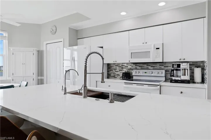 Kitchen with white cabinetry, a kitchen breakfast bar, white appliances, and light stone counters