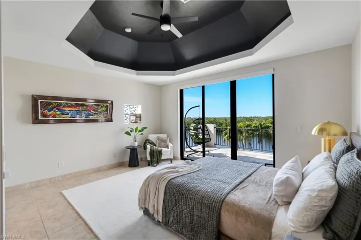 Bedroom featuring a raised ceiling, access to outside, tile patterned flooring, a ceiling fan, and a water view
