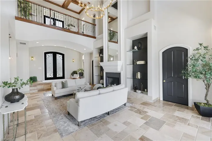 Living room with built in features, a high ceiling, arched walkways, stone tile flooring, and a chandelier