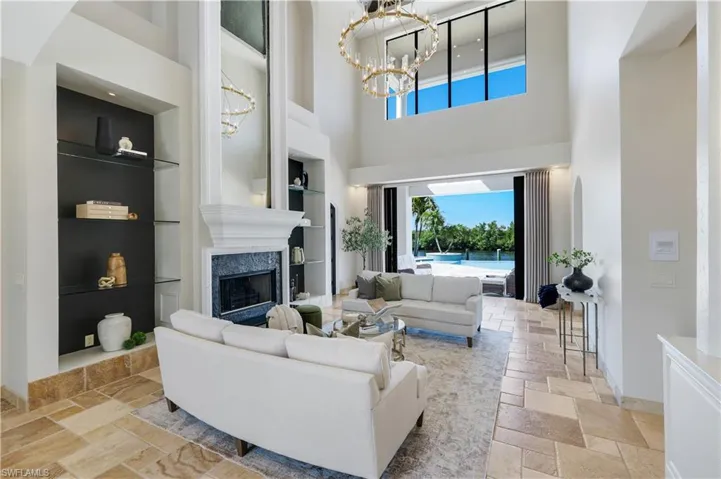 Living room featuring stone tile flooring, built in features, hanging lights, a high ceiling, and a fireplace