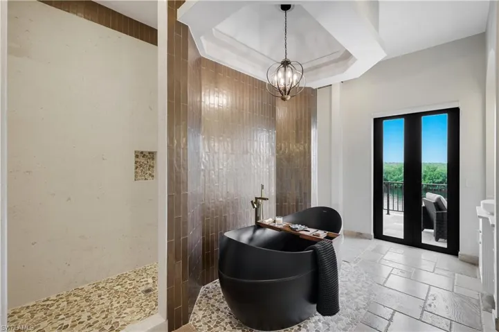 Full bath featuring stone tile floors, a chandelier, a soaking tub, a raised ceiling, and a walk in shower