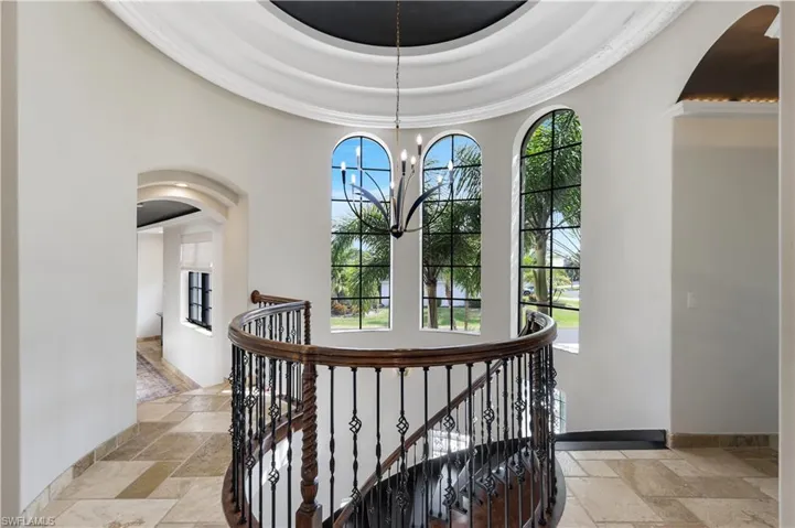 Hall featuring stone tile floors, arched walkways, an upstairs landing, and a chandelier