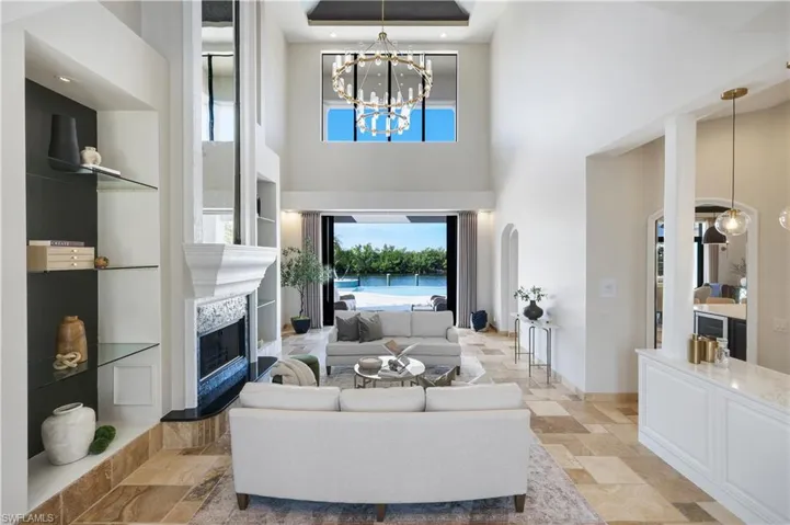 Living room with a chandelier, stone tile flooring, a high end fireplace, and a high ceiling