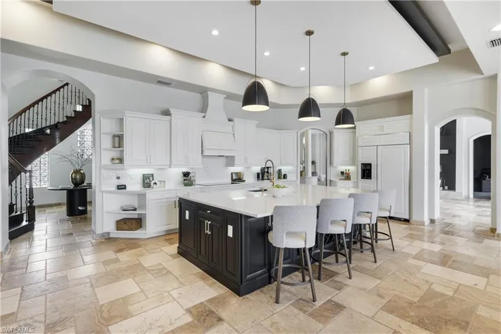 Kitchen with arched walkways, open shelves, dual tone cabinets, a large island, and light stone counters