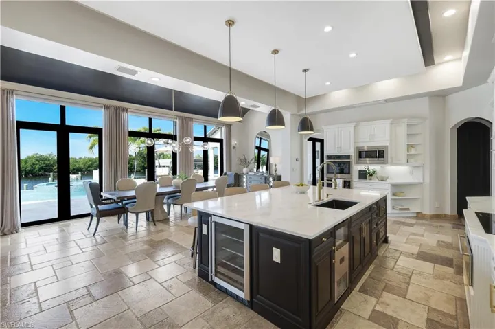 Kitchen with arched walkways, dual tone cabinets, light stone counters, open shelves, and a tray ceiling