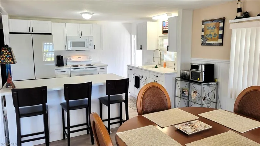 Kitchen with white cabinetry, a breakfast bar, white appliances, and light countertops