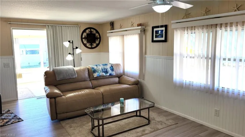 Living room featuring healthy amount of natural light, wood walls, wood finished floors, and a ceiling fan