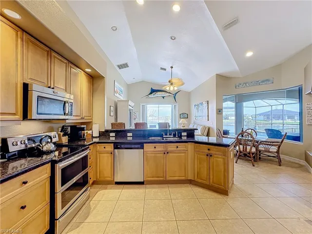 Kitchen featuring stainless steel appliances, lofted ceiling, light tile patterned floors, recessed lighting, and dark stone counters