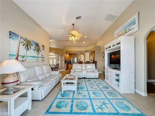 Living area featuring arched walkways, a ceiling fan, light tile patterned floors, and vaulted ceiling