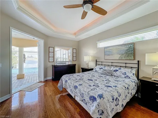 Bedroom featuring access to outside, a tray ceiling, dark wood-style floors, multiple windows, and crown molding
