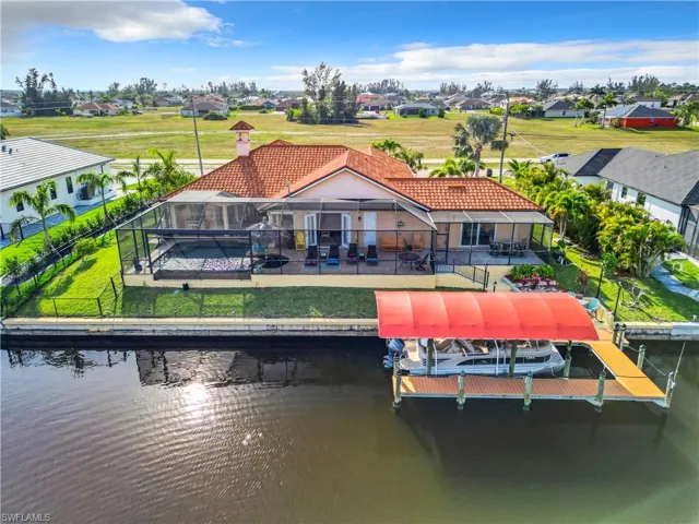 Rear view of house featuring boat lift, a sun deck, a lanai, a patio, and an intersecting canal view