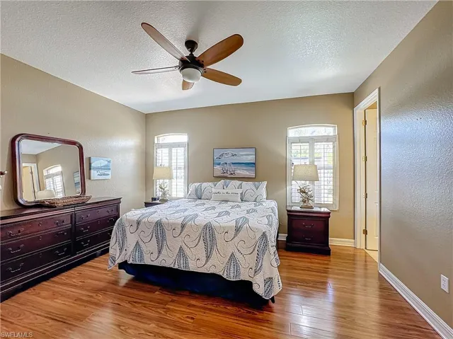 , Bedroom with ensuite bathroom a textured ceiling, dark wood finished floors, multiple windows, and a ceiling fan