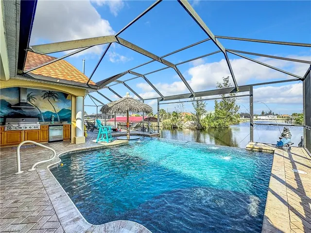 Swimming pool featuring a sunroom, an outdoor kitchen, a lanai, a patio, and a water view