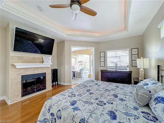 Bedroom with a raised ceiling, wood finished floors, a fireplace, and a ceiling fan