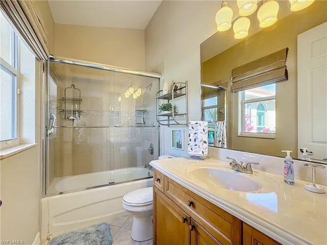Full ensuite  bath with vanity, light tile patterned floors, and bath / shower combo with glass door