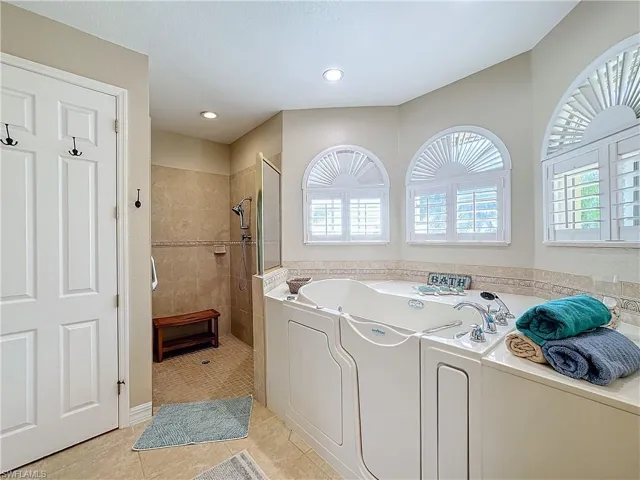 Bathroom with a garden tub, light tile patterned flooring, and tiled shower