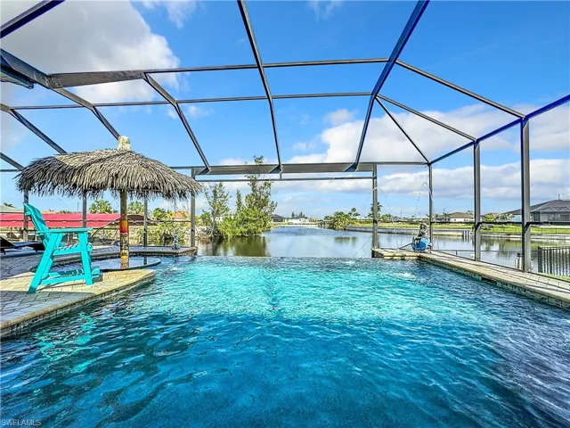 Infinity edge Swimming pool featuring a sunroom, glass enclosure, a water view, and a residential view