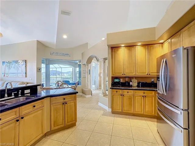 Kitchen featuring stainless steel refrigerator with ice dispenser, arched walkways, dark stone countertops, light tile patterned floors, and ornate columns
